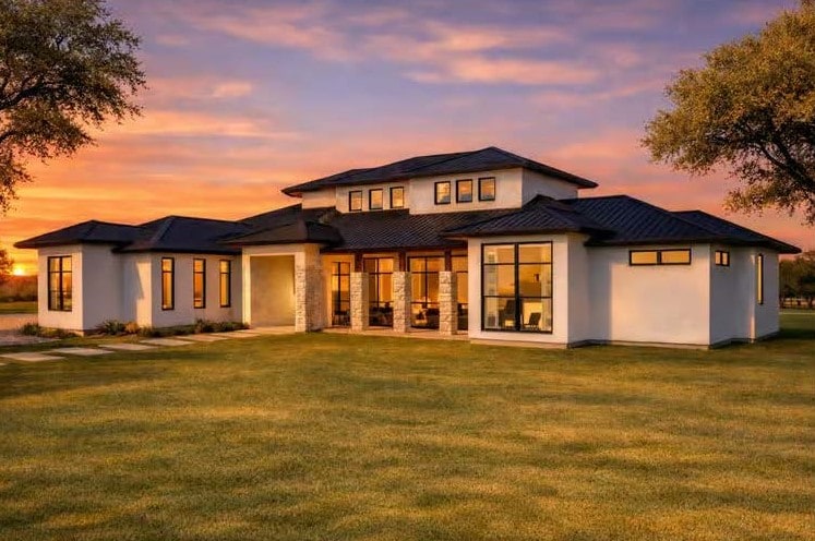 The Monaco — three-quarter exterior at sunset, with warm interior light behind the window walls