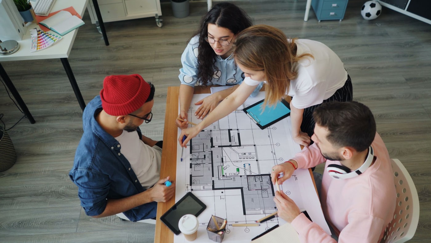 Overhead photograph of a team reviewing a floor plan blueprint together at a table — representing project planning and direction