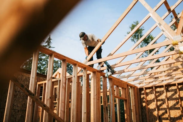 Photograph of a construction worker framing a roof structure on a job site — representing active construction and execution