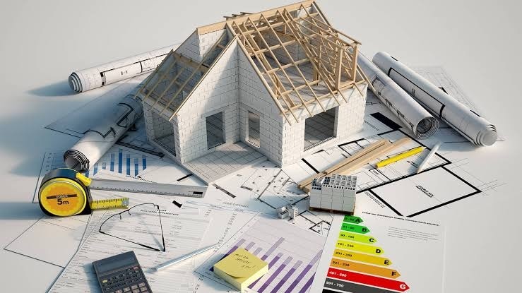 Photograph of a 3D home model staged among blueprints and planning tools — representing project renderings and progress visibility